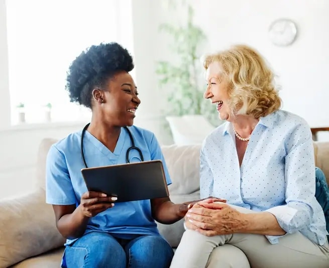 Nurse caregiver holding tablet smiling with senior woman 1