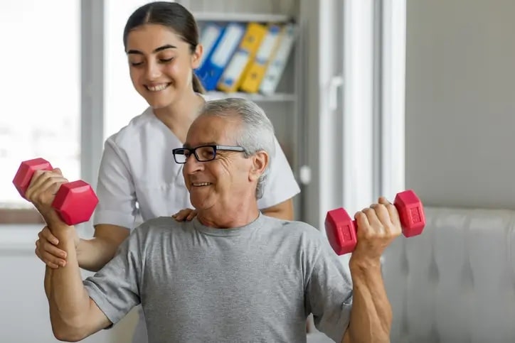 Skilled nurse and senior patient using dumbells for short term rehabilitation exercises